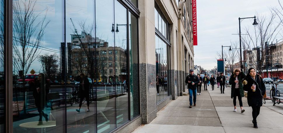 Photo: On the left, a glass wall of a BU building on 808 Commonwealth Ave. There are students walking on the sidewalk on the right. They are wearing winter coats, indicating it's cold outside.