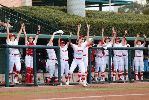 Photo: The BU Women's Softball team, wearing white and red jerseys, celebrates in the dugout during a recent game