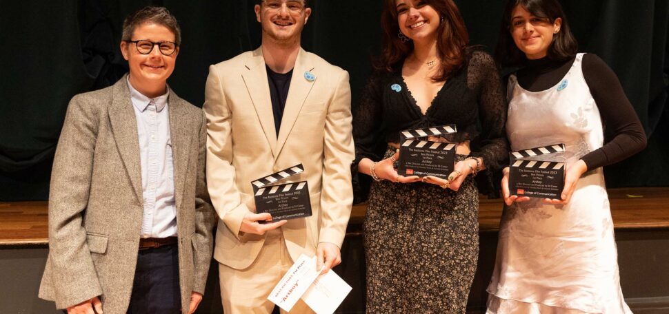Photo: A group shot of the winners of the Redstone Film Festival. From left, a short white man in a gray blazer and a blue button-up dress shirt. Next, a taller Southern Asian man in a stream-lined tan suit and a black t-shirt. Next to him, a Southern Asian woman in a black, lace top and a floral maxi skirt. And lastly, the person on the right is a Sourthern Asian woman with a black mock-neck top and a silk, grey dress.