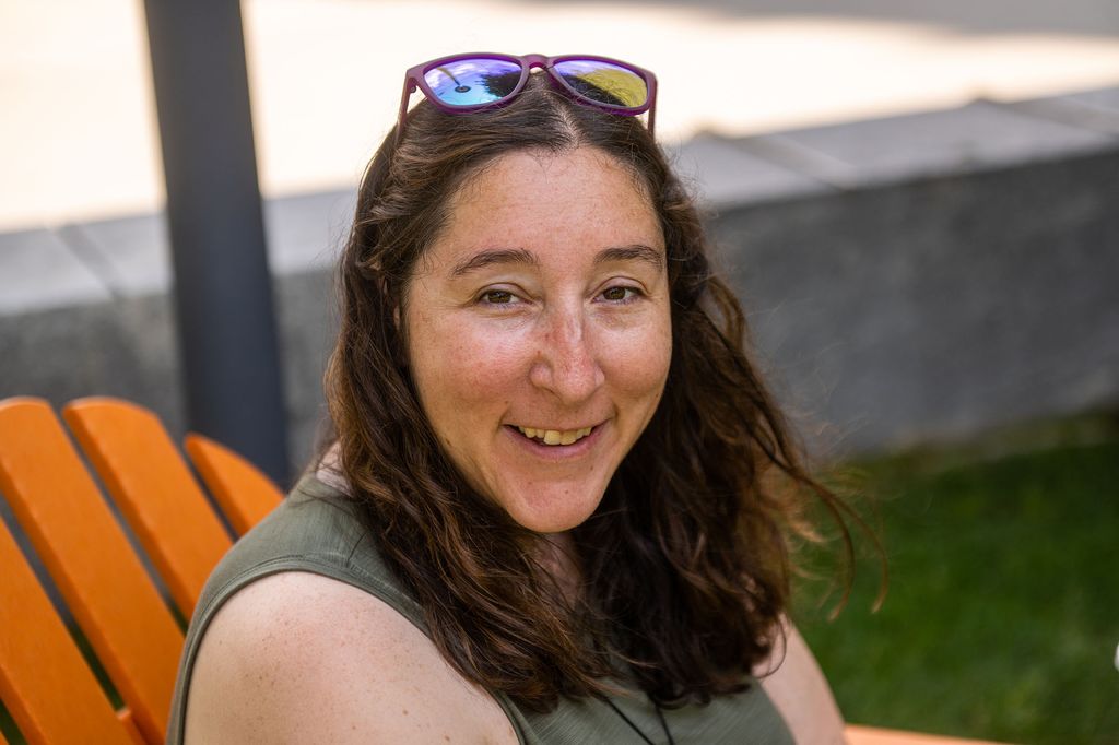 Photo: A young white woman with brown hair and wearing a green shirt smiles for the camera s as sits in an orange lawn chair.