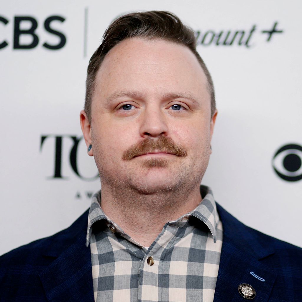 Photo: A white man with a moustache smiles at the camera. Alex Neumann attends the 76th Annual Tony Awards Meet The Nominees press event in New York on May 04, 2023. (Photo by Leonardo Munoz / AFP) (Photo by LEONARDO MUNOZ/AFP via Getty Images)