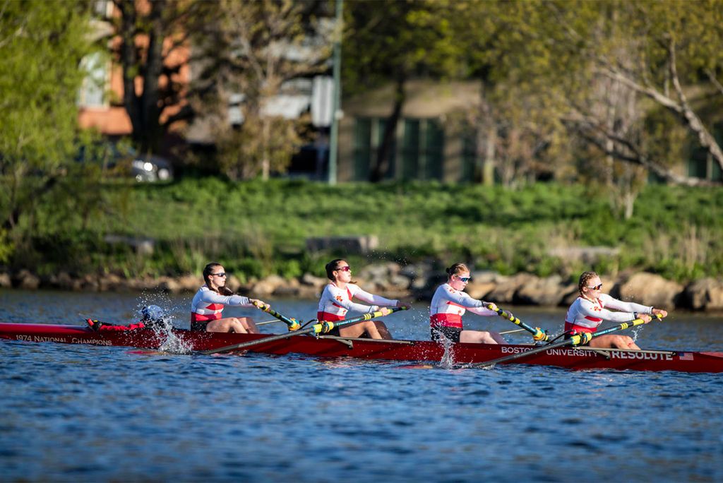 Photo: A group of women row a large boat with oars, they are all wearing matching red uniforms and tank tops