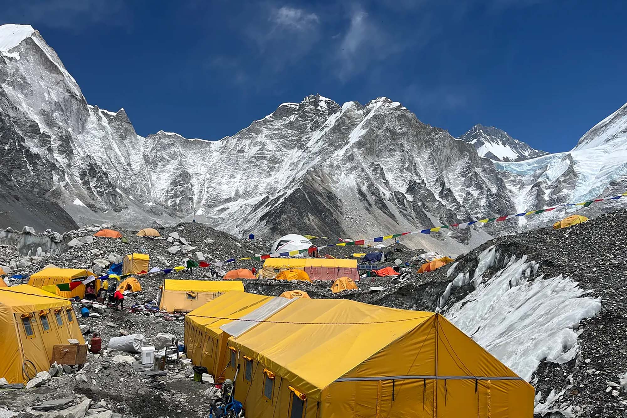 Photo: Photo: A horizontal shot of a base camp on Mt. Everest. Snow covers the ground and the elevated areas. On top of the snow are various yellow tents making up the base camp. The sky is bright and blue.