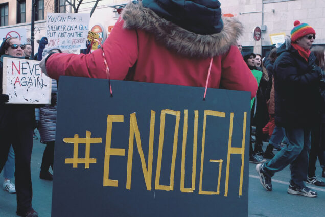 Photo: A navy blue with gold lettering sign of #ENOUGH at a no guns protest in 2018.
