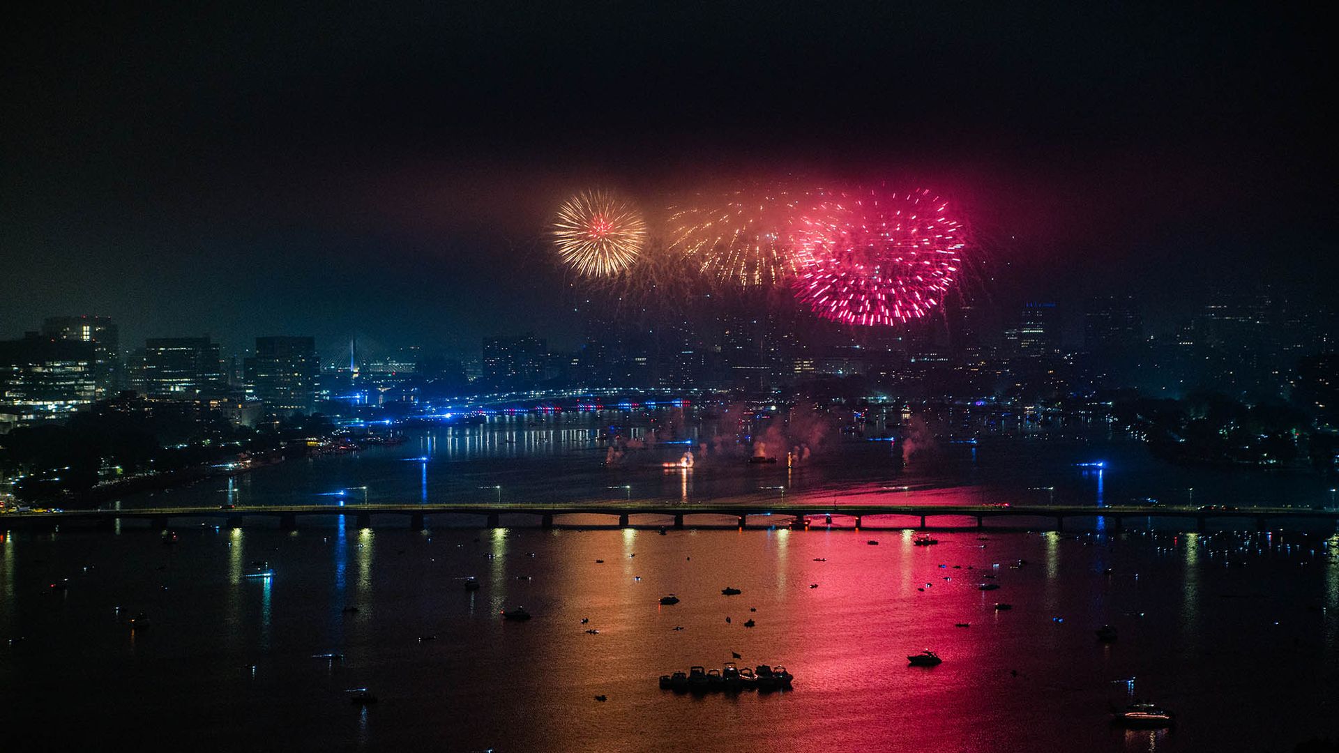 Photo: 4th of July fireworks are shown going off on a dark night above the Charles river. bright pink, orange, and white fireworks light up the night sky and show the Boston skyline.