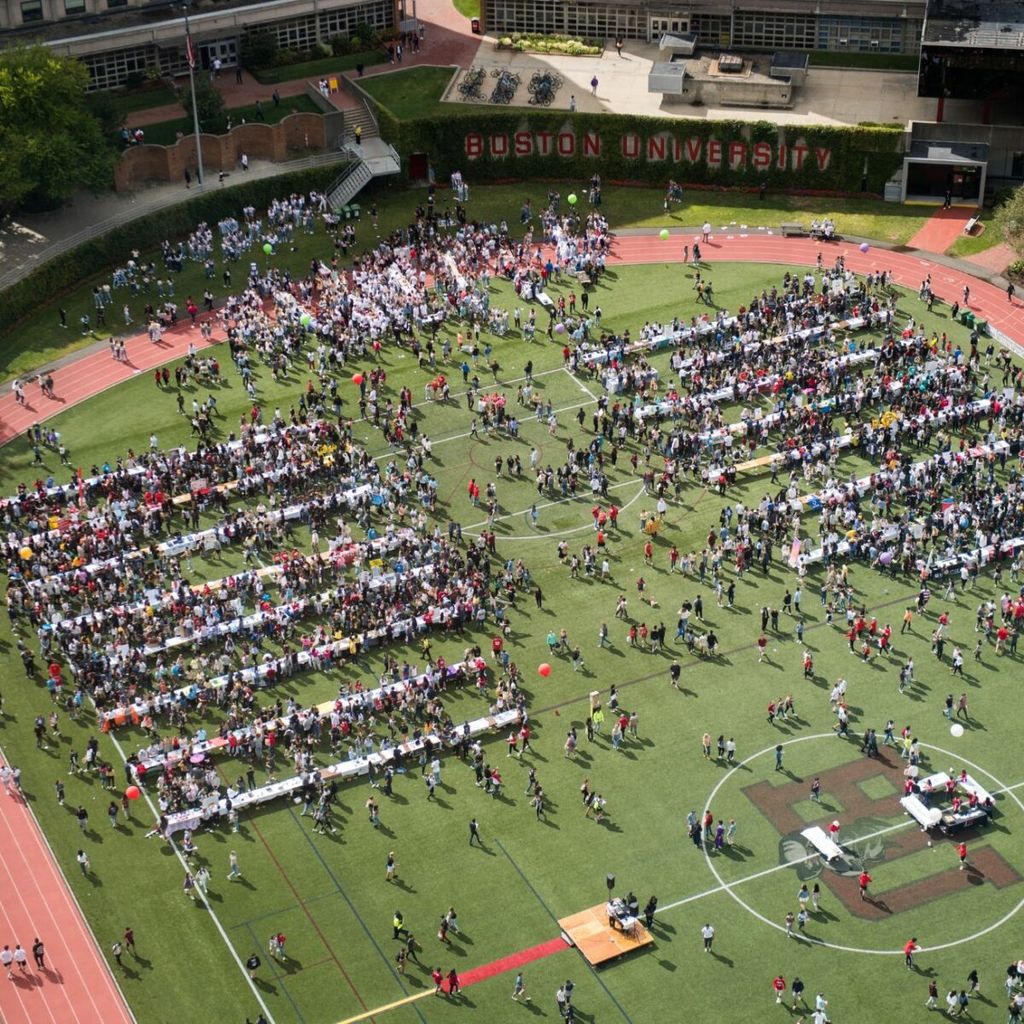 This is a bird's eye view of Nickerson Field during SPLASH. There are tables scattered down the field, with people crowded around each table. There are lots of students crowding towards the inner tables. 