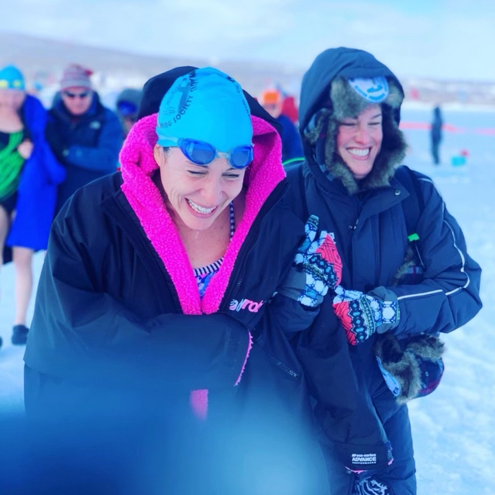 Photo: Craigen (left) smiles and huddles under a large black winter coat. To her right, a friend smiles as she's bundled up in full winter gear and ski goggles. They both walk in a snowy field.