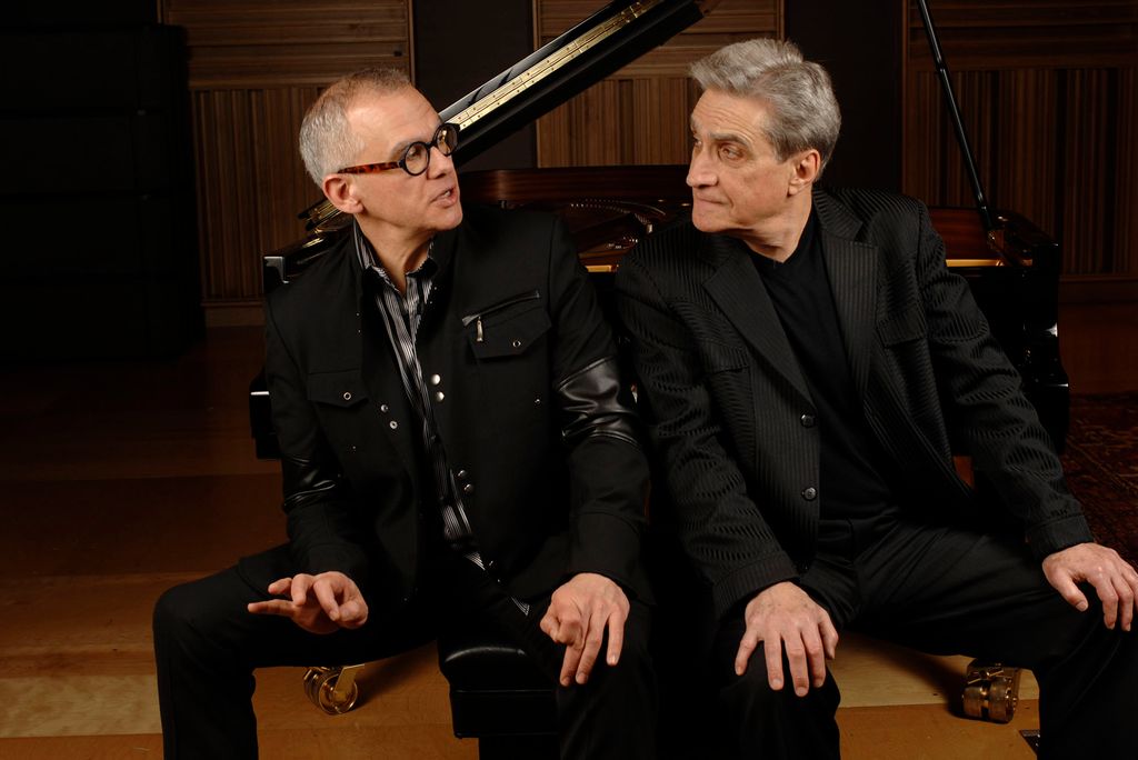 Photo: Two men, Laurence Hobgood and Robert Pinsky, sit next to each other on a wooden stage, both dressed in all black garb. The face one another, immersed in conversation.