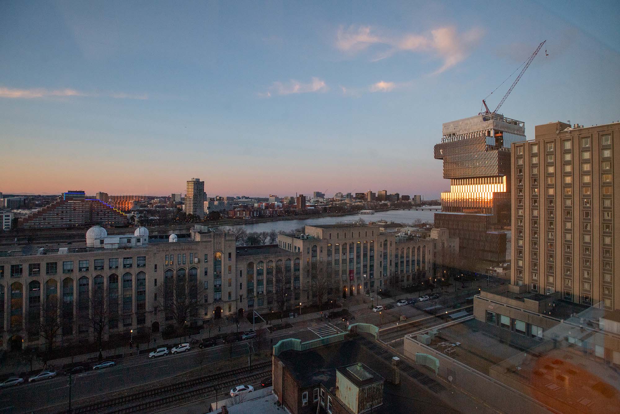 Photo of the Boston University campus, including the Center for data Science, from the top of the Photonics building. Campus view is seen during sunset, with orange and purple hues in the sky fading to a darkish blue.