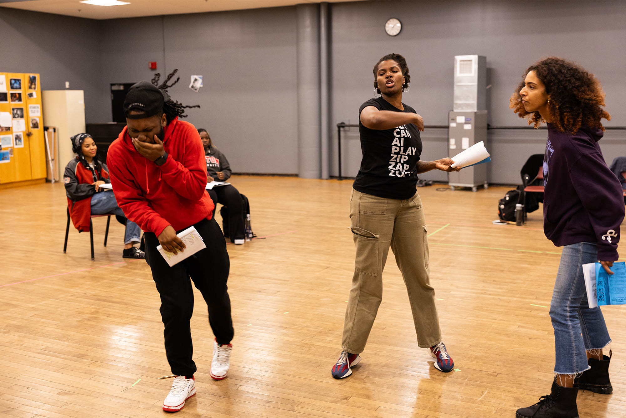 Photo: Two college students acting in a room with a wooden floor while other classmates watch their scene
