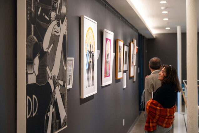 Photo: Patrons look towards the large artwork displayed on the dark walls of a gallery.