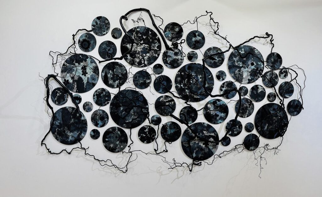 Photo: Image shows abstract artwork of monotype on Hahnemuhle paper on aluminum. Black circles of various sizes are placed on a wall and connected by thin black wires.