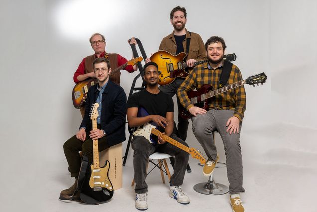 Photo: Group photo of five men sitting and standing. They all hold guitars. From left: Nathaniel Braddock, Brian Barrone, Kumera Zekarias, Erik Broess, and Lance Morrison.