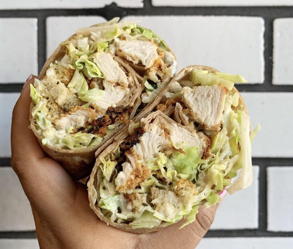 Photo: A hand holding a wrap sandwich with chicken, lettuce and sauce