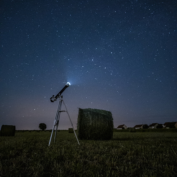 Photo: A lone telescope is shown aimed at a starry night sky in an open field.