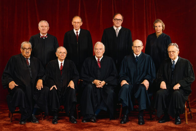 Photo: Group photo of the Supreme Court when Sandra Day O'Connor joined. A group of people wearing Black Supreme Court robes stand and sit in front of dark red curtain. The Justices are (left to right front row;) Thurgood Marshall; William J. Brennan Jr.; Chief Justice Warren Burger; Byron R. White; Harry A. Blackmun. (Back row, left to right;) John Paul Stevens; Lewis F. Powell, Jr.; William H. Rehnquist; Sandra Day O'Connor.