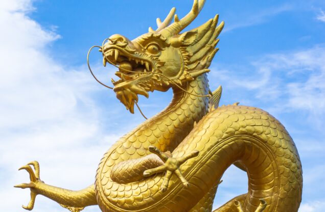 Stock photo courtesy of Canva. The photo is of a golden dragon statue with a blue sky in the background. There are light clouds lining the sky.