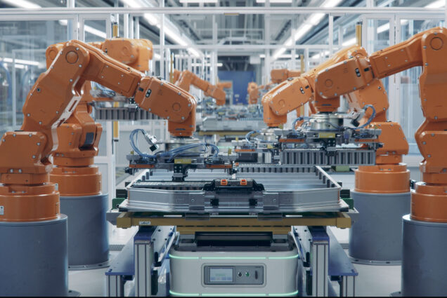 Photo: A set of 4 large orange robotic arms assembling a large electric car battery on a production line