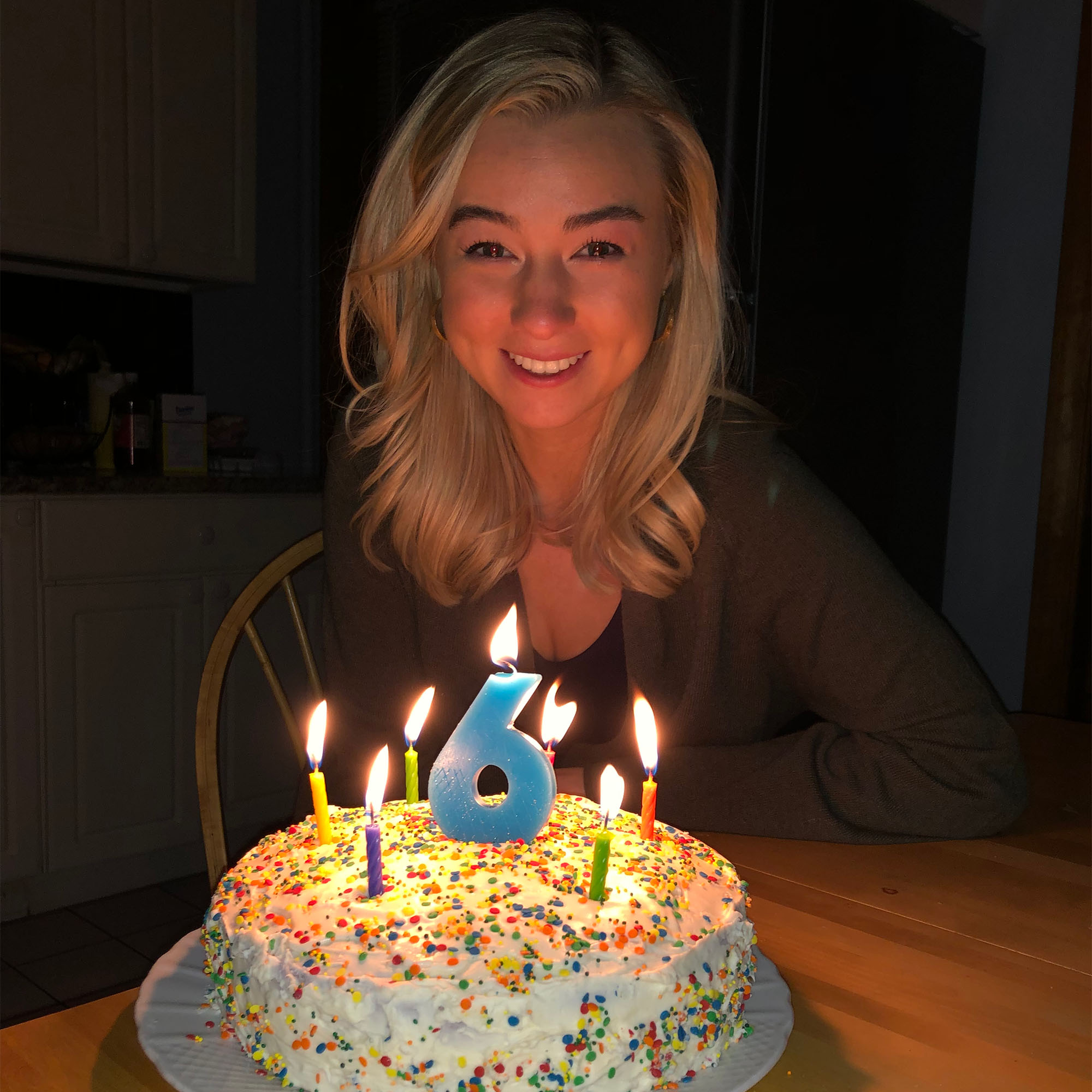 Photo: A young blonde woman in front of a cake with a large #6 candle on it