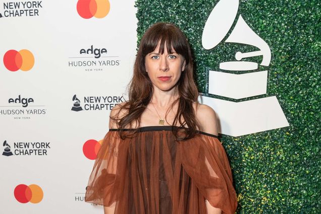 Photo: A woman in an elegant flowing dress stands in front of a photoboard at the 2024 Grammys