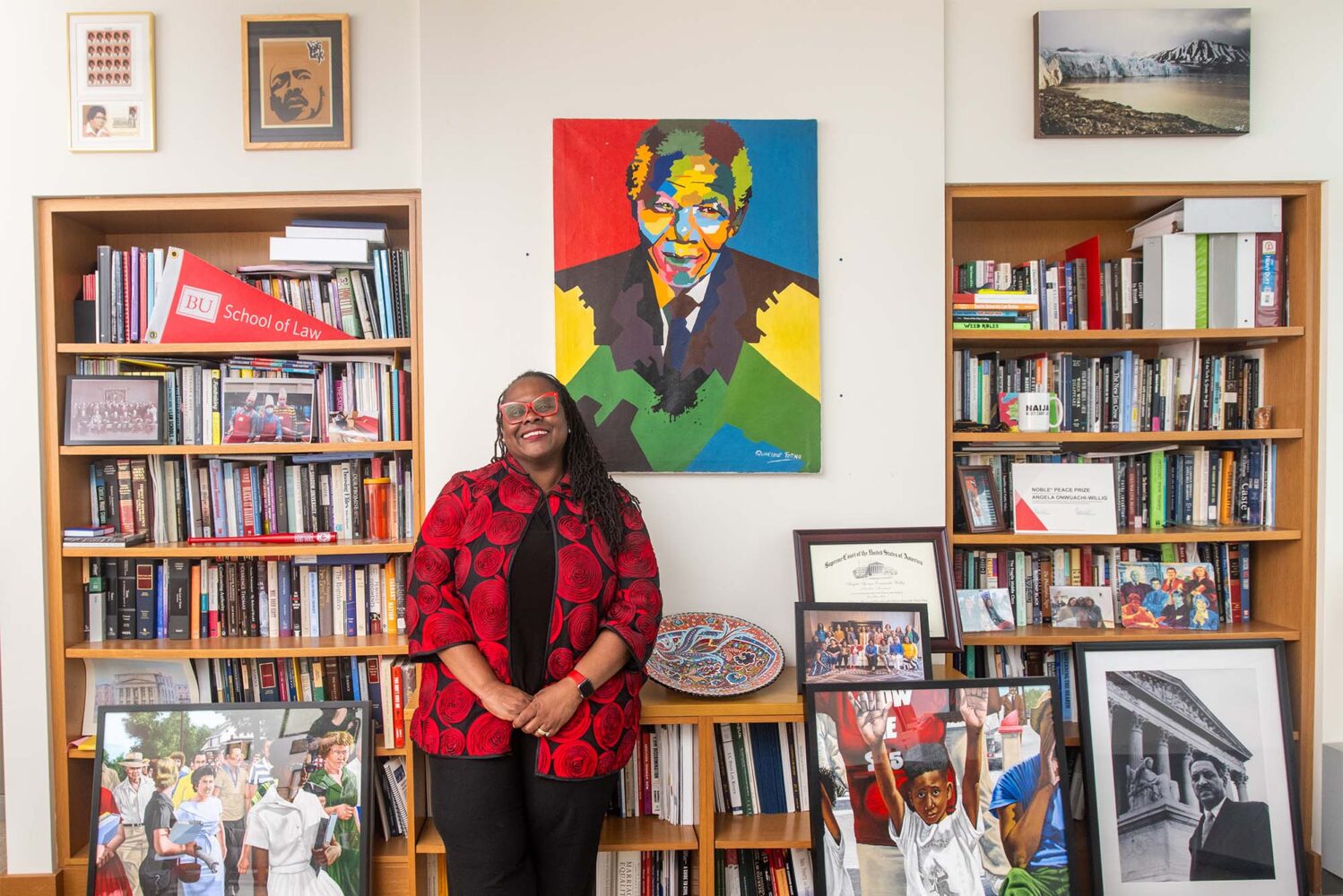 Photo: A black woman wearing a colorful cardigan in front of a wall of bookcases and art