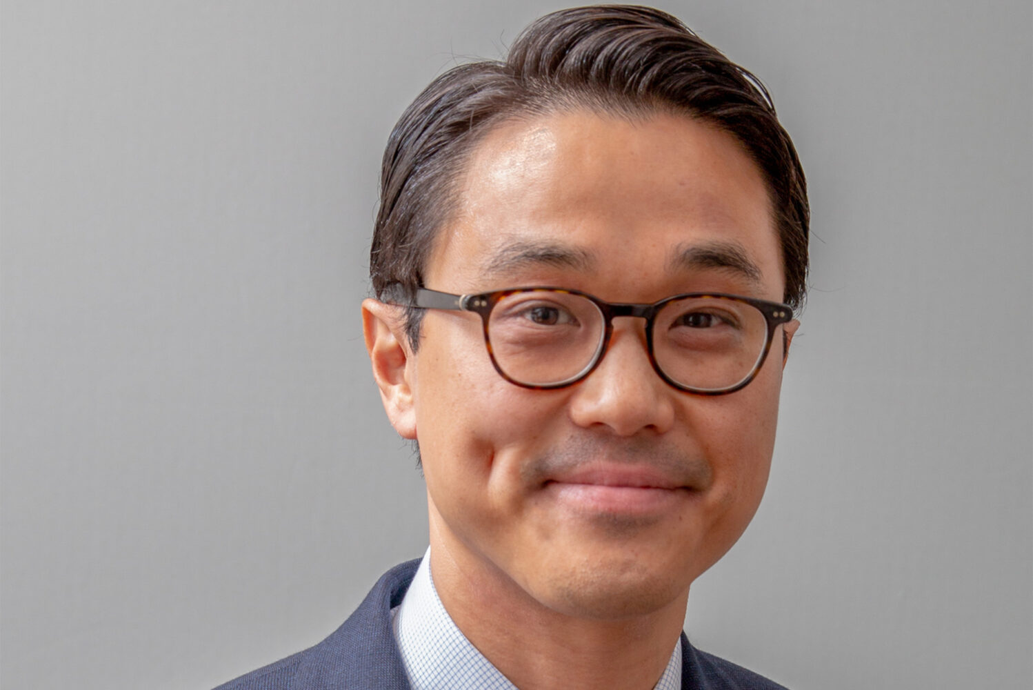 Photo: An asian man wearing a collared shirt and suit with glasses and a soft smile