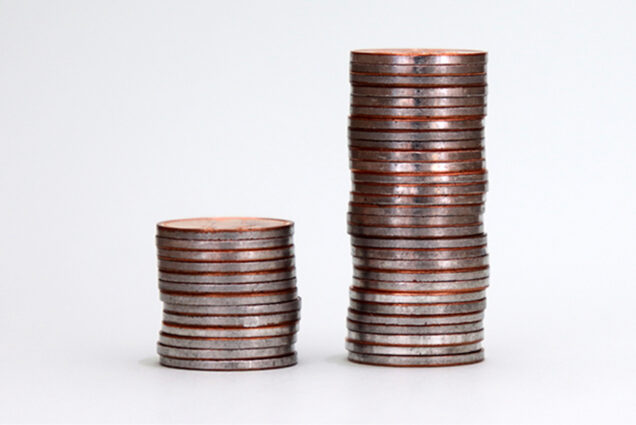 Photo: Two stacks of coins, one large and one small. Depicts wealth inequality