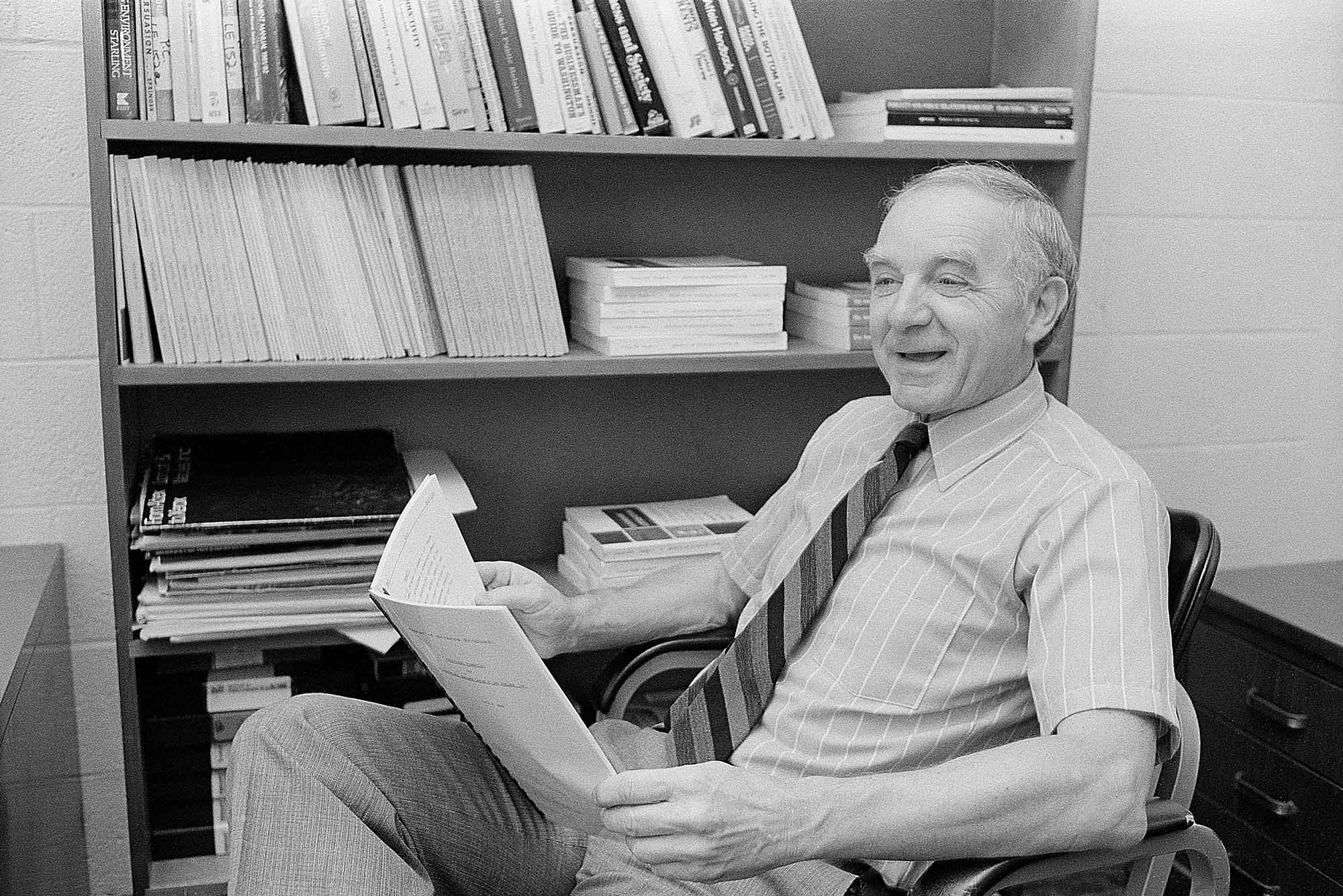 Photo: A black and white photo of Otto Lerbinger, a white balding man, sitting at his desk with papers, looking off to something else behind the camera.