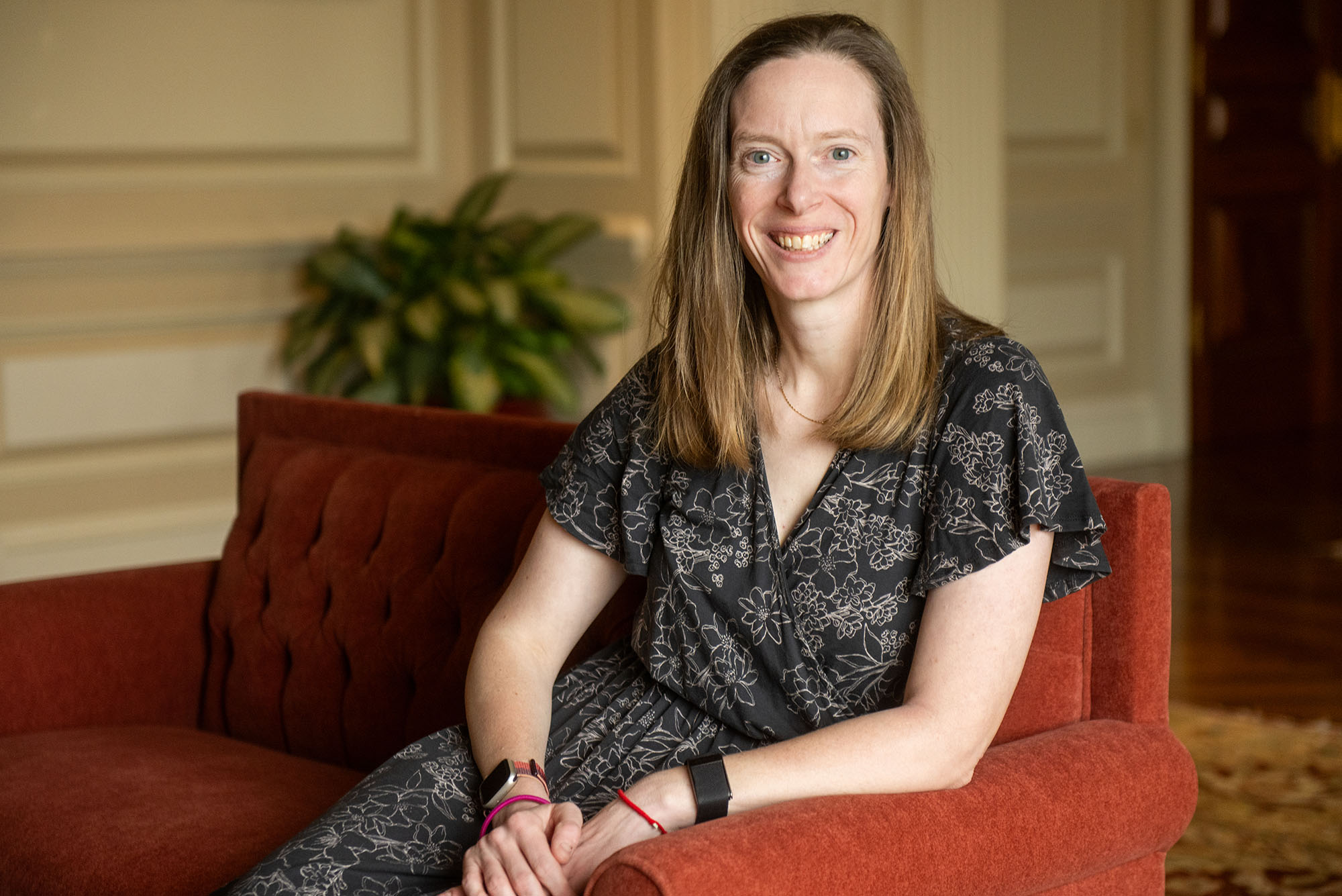 Photo: A white woman with a black and white jumpsuit sits on the couch while smiling.