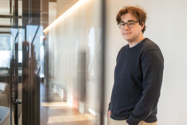 Photo: A picture of a man standing with his hands in his pockets. He is wearing a sweater and glasses