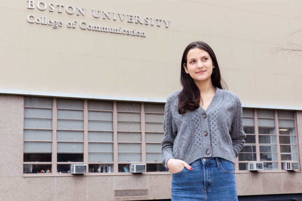 Photo: A college student with long dark hair poses in front of a large building with lettering reading "Boston University College of Communication"