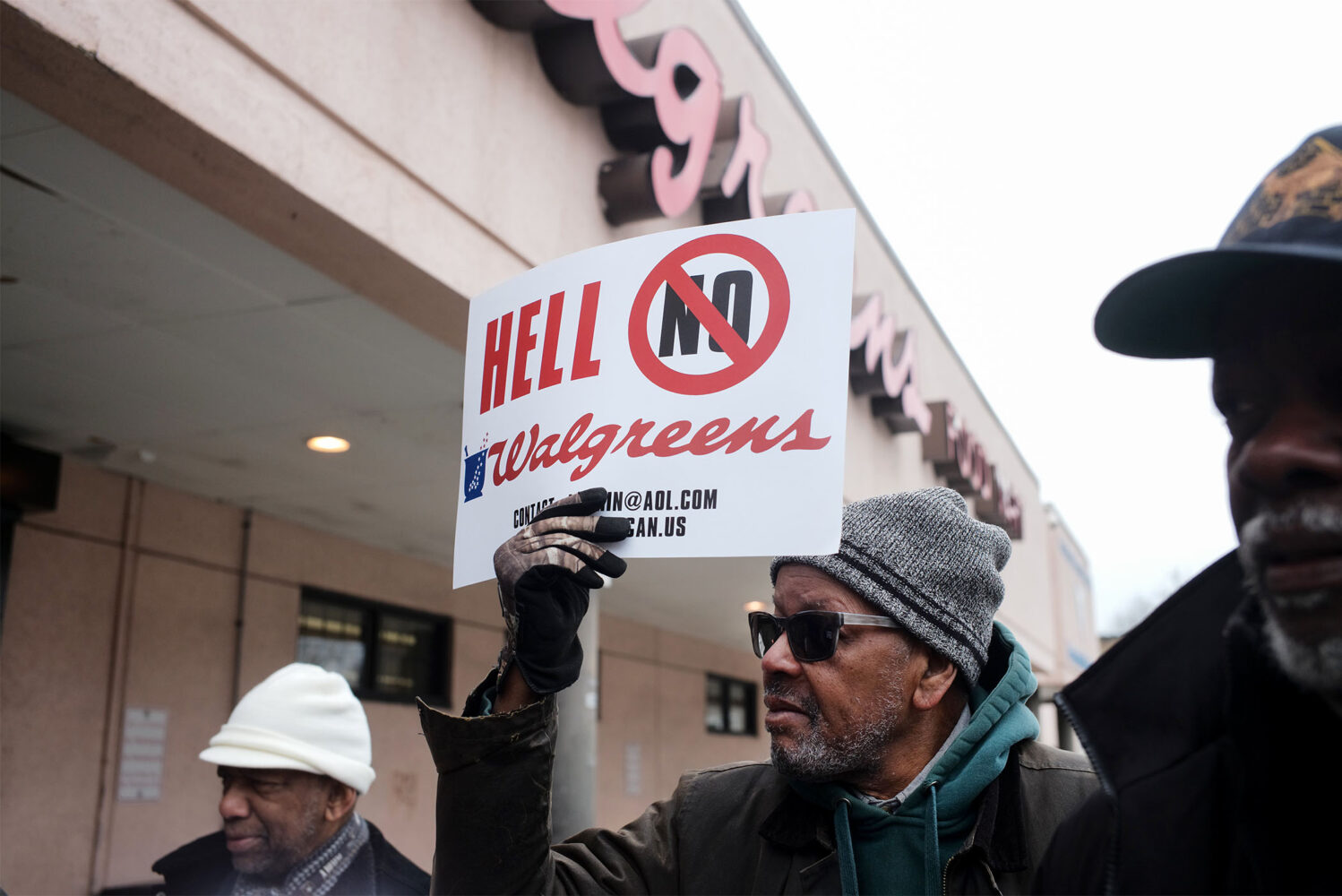 Photo: A group of men protesting outside of a Walgreens. The one in the middle is holding a sign that says "Hell No Walgreens" with a circle and a line over the "No"