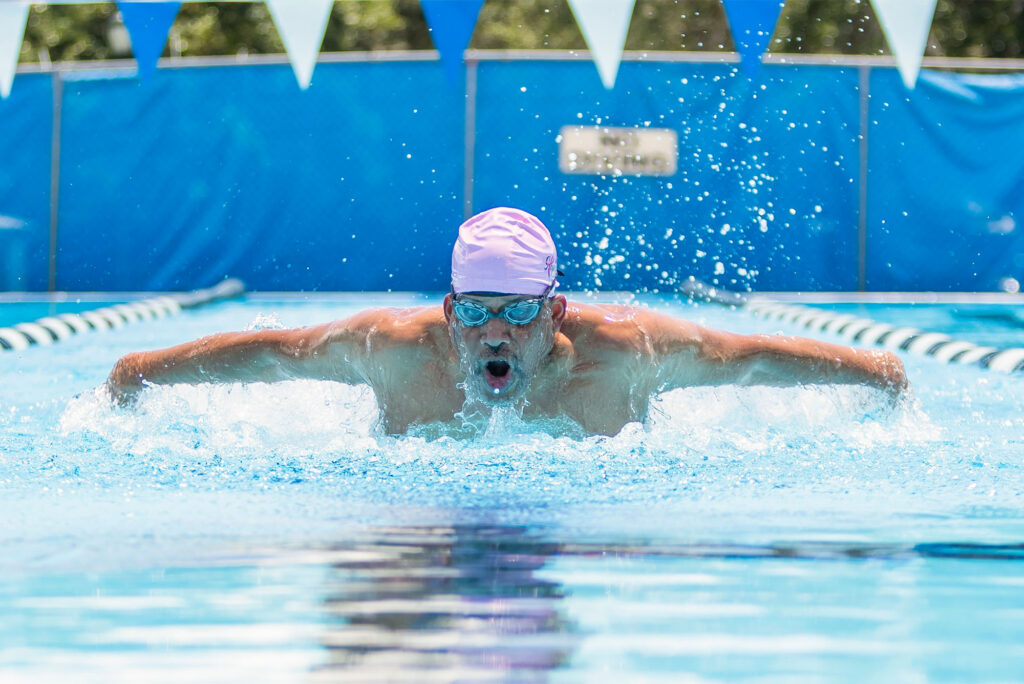 Photo: An older man wearing a swim cap and googles mid swimming stroke in a large pool