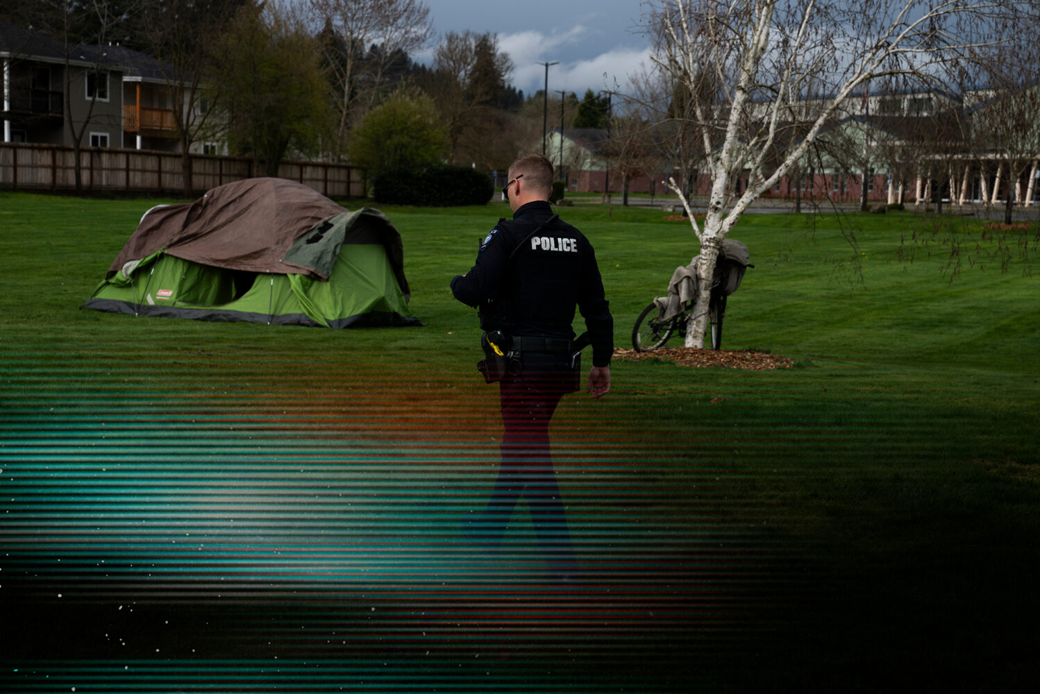 Photo: A picture of a man in a police uniform walking through a field that has a tent. There is a glitch overlay over the image