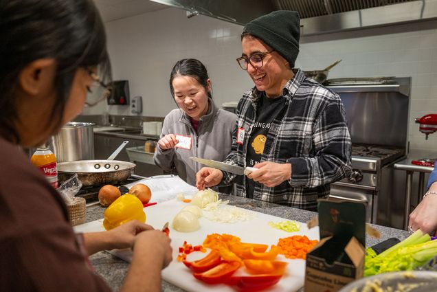 Photo: A picture of three people gathered around a cutting board and chopping onions and peppers