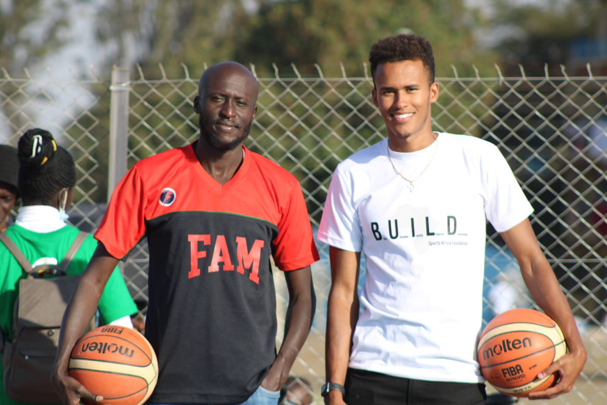 Photo: A picture of two men posing for the camera. Both are holding basketballs and the one on the right has on a shirt with the acronym "B.U.I.L.D."