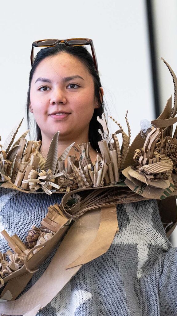 Photo: A picture of a girl wearing a gray sweater with white stars and a cardboard sculpture around her neck. The sculpture sits almost like a scarf and features 3D elements