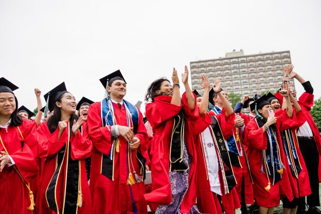 Photo: A sea of Boston University graduates in red gowns sit on Nickerson Field at the 151st Commencement in 2024. There is a white play button overlaid on top of the image.