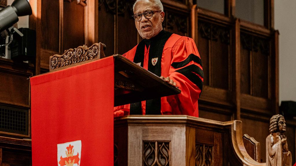 Photo: A man in a red gown gives a speech at a podium draped in a red covering. Baccalaureate speaker Walter E. Fluker (GRS’88, STH’88) told Boston University’s Class of 2024 graduates Sunday to follow the example of BU’s most famous alumnus, Martin Luther King, Jr., in striving for peace and justice. Photo by Kelly Davidson