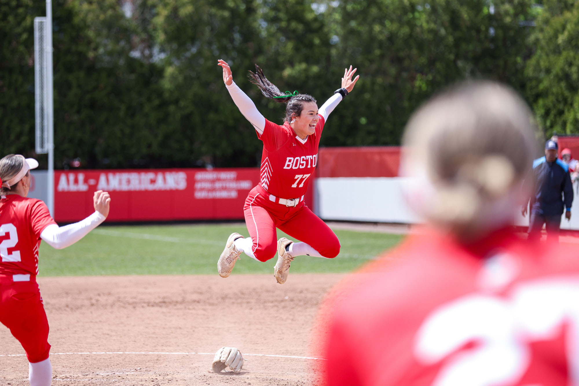 Photo: A picture of a girl in a red softball uniform with white accents jumping on the field in excitement