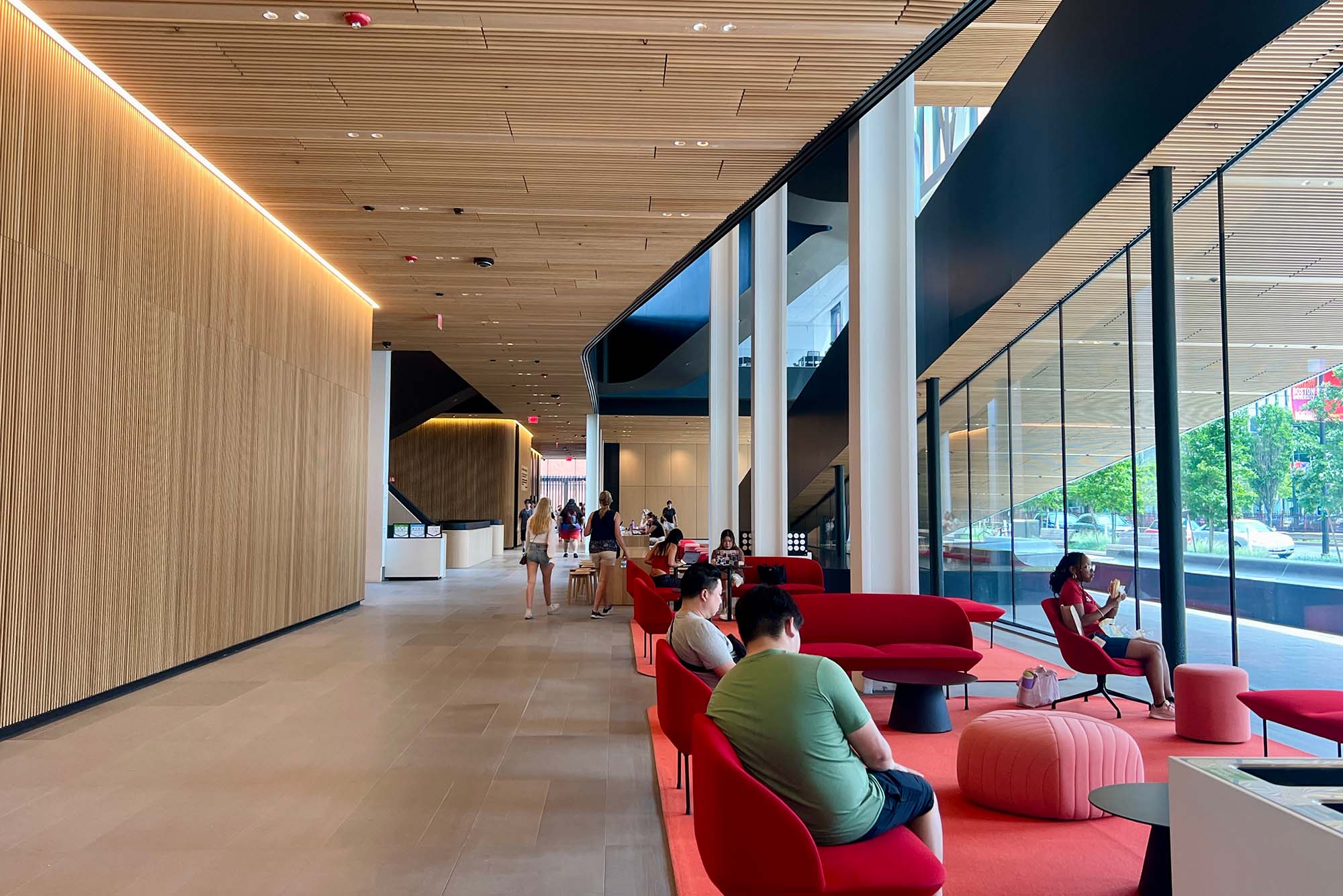 Photo: A picture of the inside of a college academic building with plush red chairs where students are working