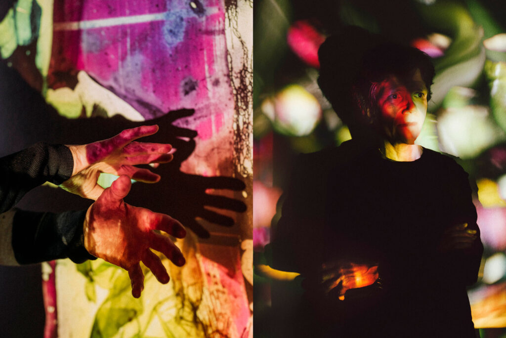 Photo: A picture of two images, both with colorful, artistic lighting. On the left is a pair of hands and on the right is a man posing in a long-sleeved black top with his arms crossed