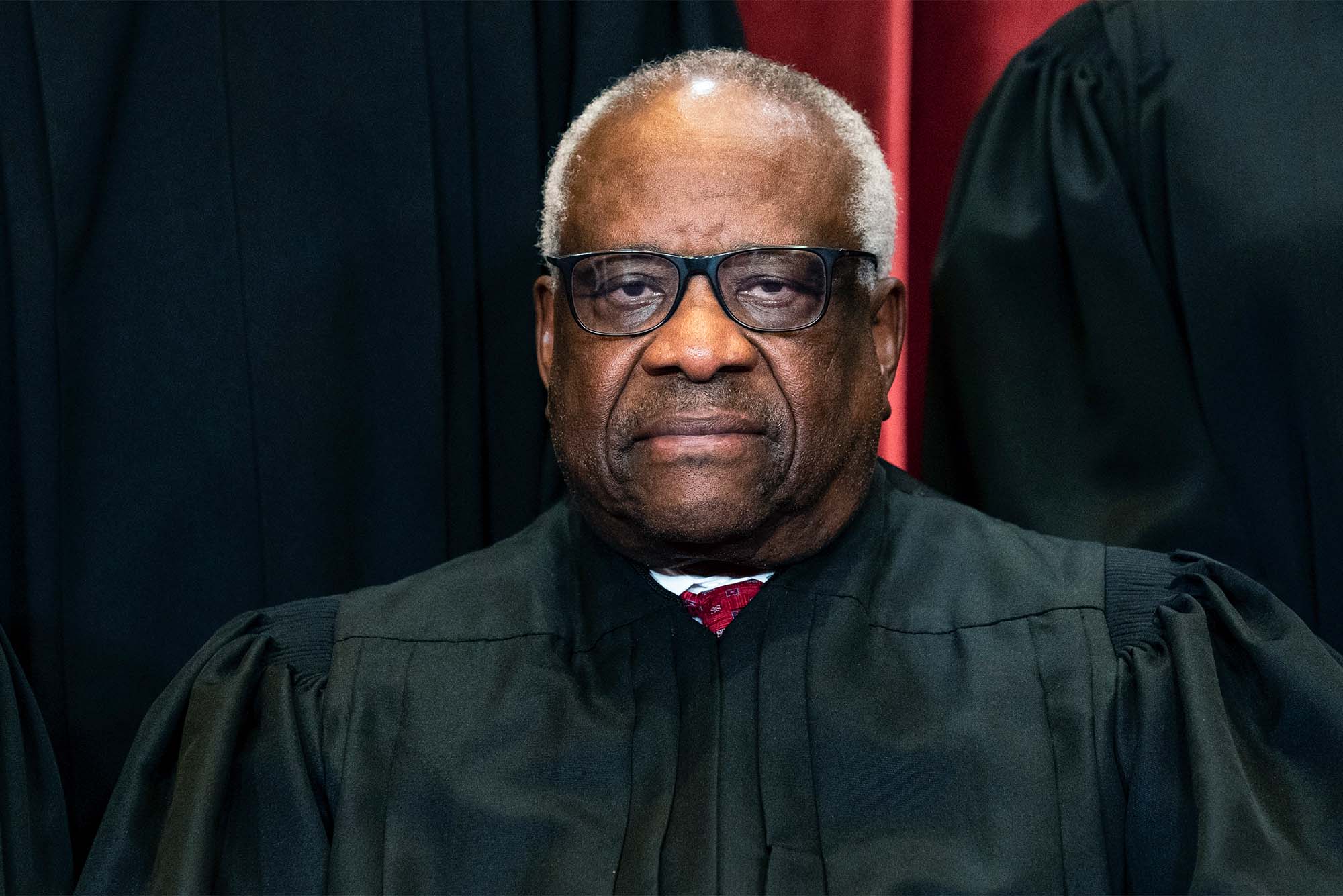 Photo of Clarence Thomas, US Supreme Court Justice, sitting in black robes with glasses. He is a black man with short white hair and a stoic expression