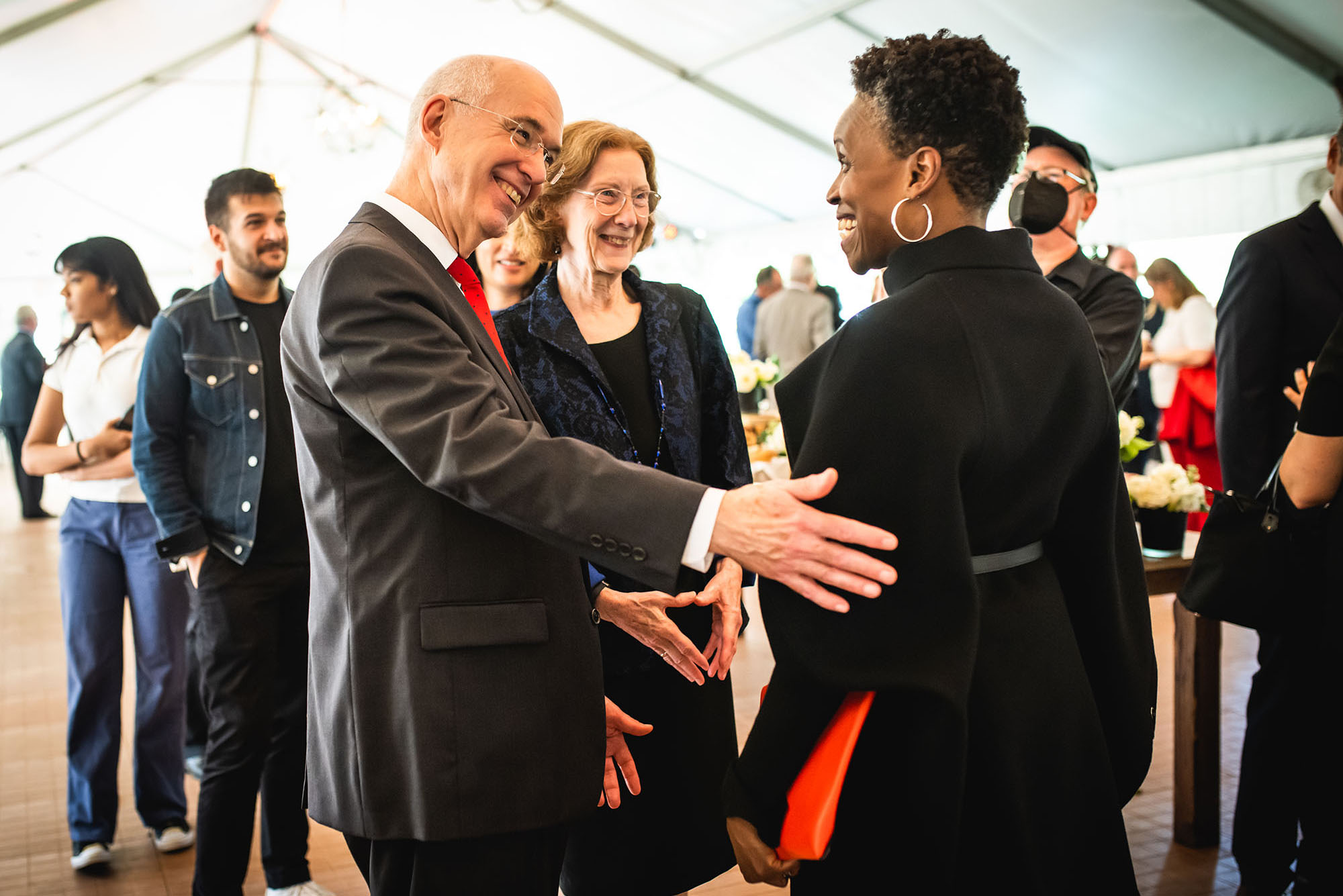 Photo: The new BU president, Melissa L. Gilliam (right), a Black woman wearing a black jacket and pants, greets Interim president Ken Freeman (left), a tall white man wearing a black suit and red tie, and his wife, Janice (center), a white woman wearing a black dress and blazer, during a reception.