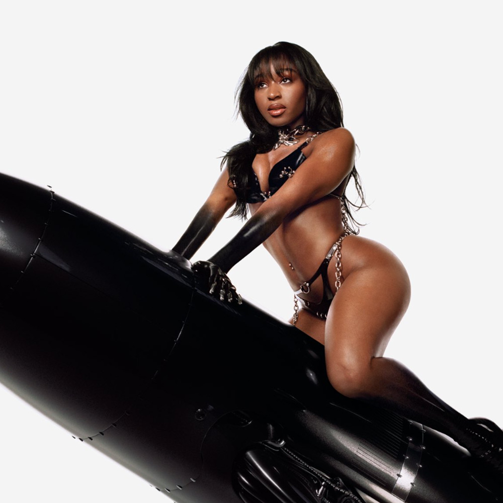 Photo: A photo of a Black women, singer Normani, on a giant black torpedo bullet. She wears nothing but a black lingerie 