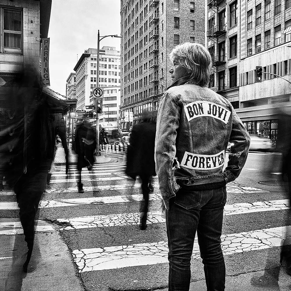Photo: A black and white shot of Bon Jovi wearing a jean jacket with his hands in his pockets, looking to the left. His jean jacket reads his name and the title of his new album, FOREVER.
