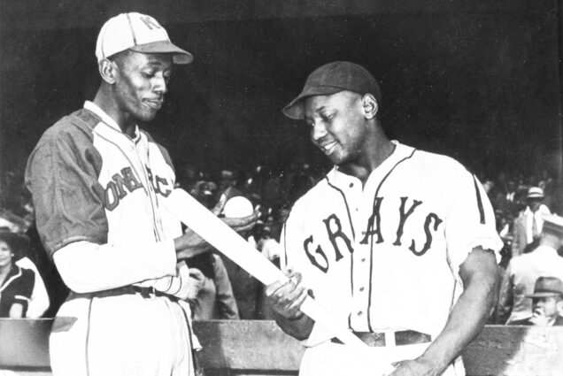 Photo: A black and white photo of two baseball players talking. The one on the right is holding a baseball bat