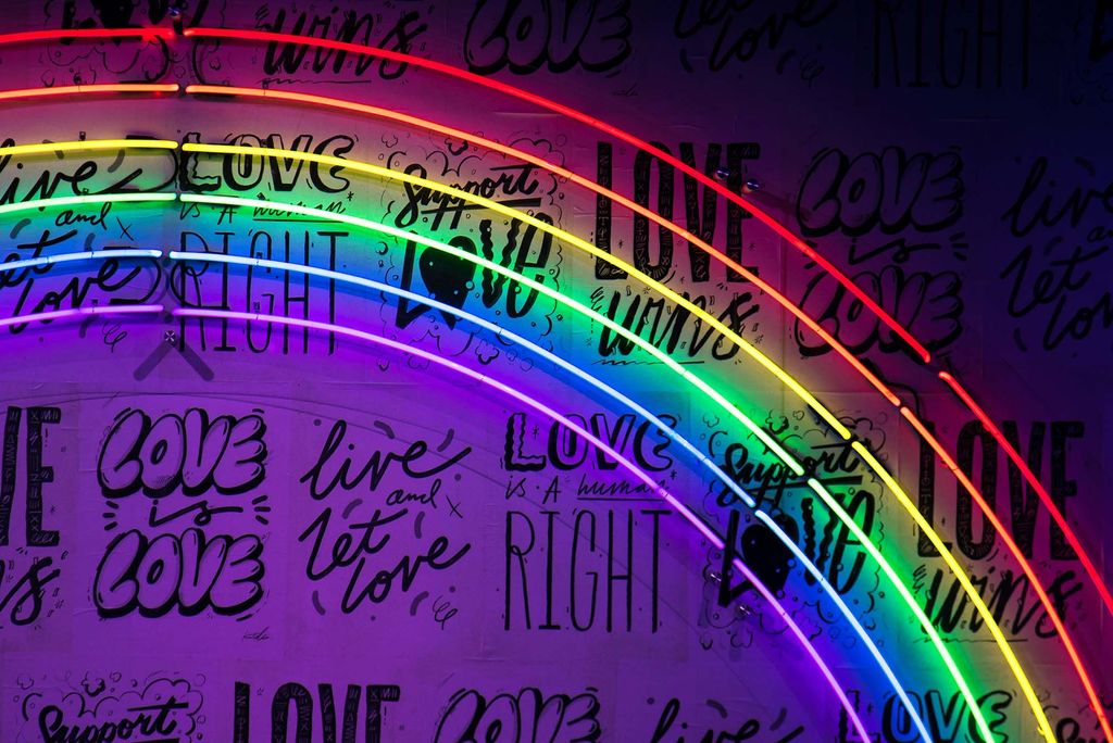 Photo: A picture of a neon rainbow sign with variations of "Love is Love" written on the wall behind it