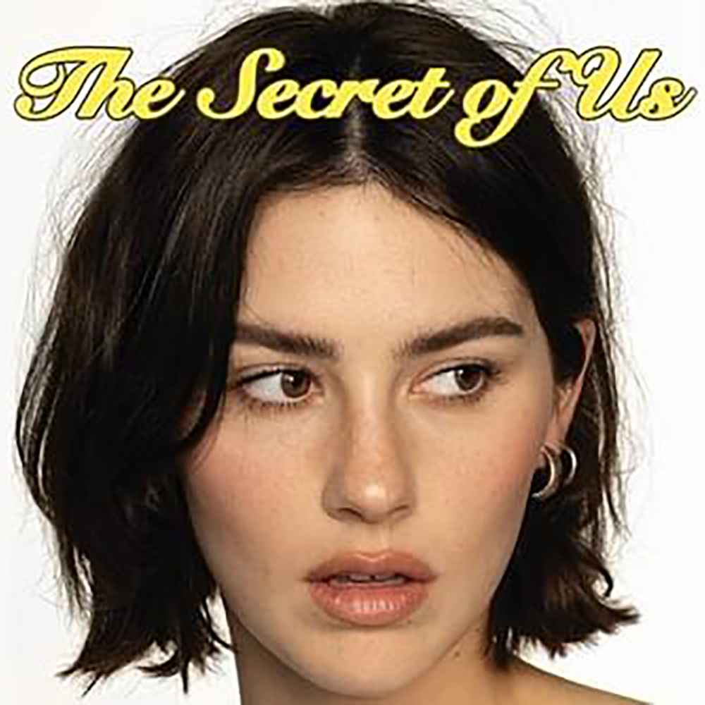 Photo: A portrait shot of a white women, Gracie Abrams, a singer with short brown hair. The text overlay over her hair reads THE SECRET OF US.
