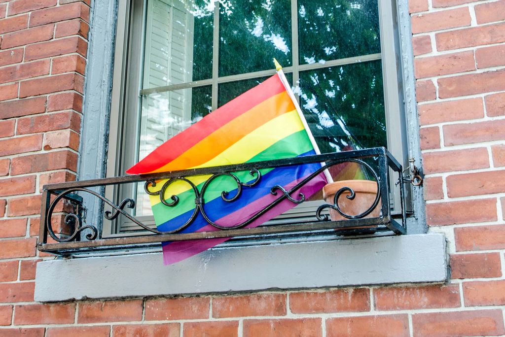 Photo: A picture of a Pride flag outside of a brownstone building's window sill 